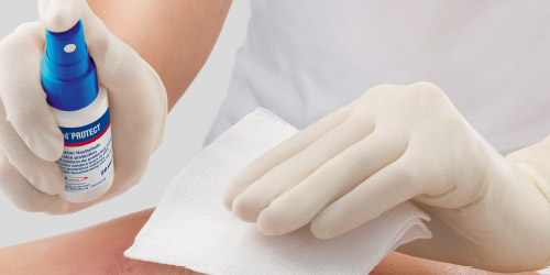 We see an HCP wearing white gloves applying a wound spray to a wound. We see an HCP wearing white gloves applying a wound spray to a wound.
